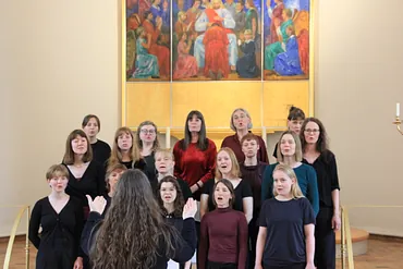 Kvinder i et sangkor foran alter og altermaleri med guldbelægning og billede af Jesus
